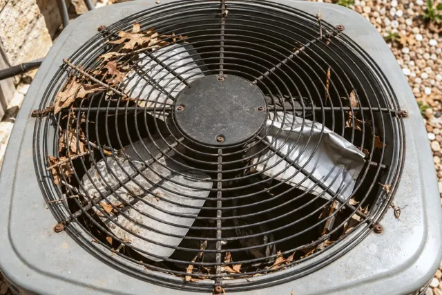 The top of an outdoor unit with a bent fan blade and leaves caught in the grille.