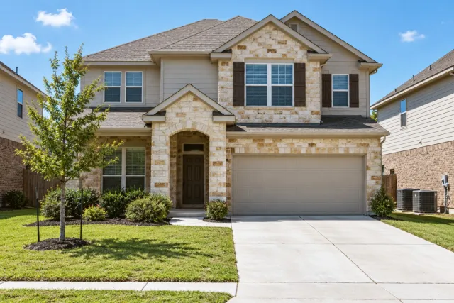 A two-storey stone-and-siding home has two outdoor units in the side yard.