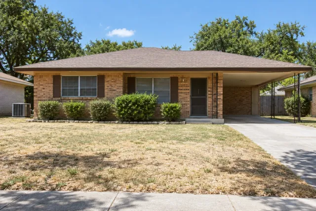 A brick ranch house with a carport has an outdoor unit beside a dry lawn.